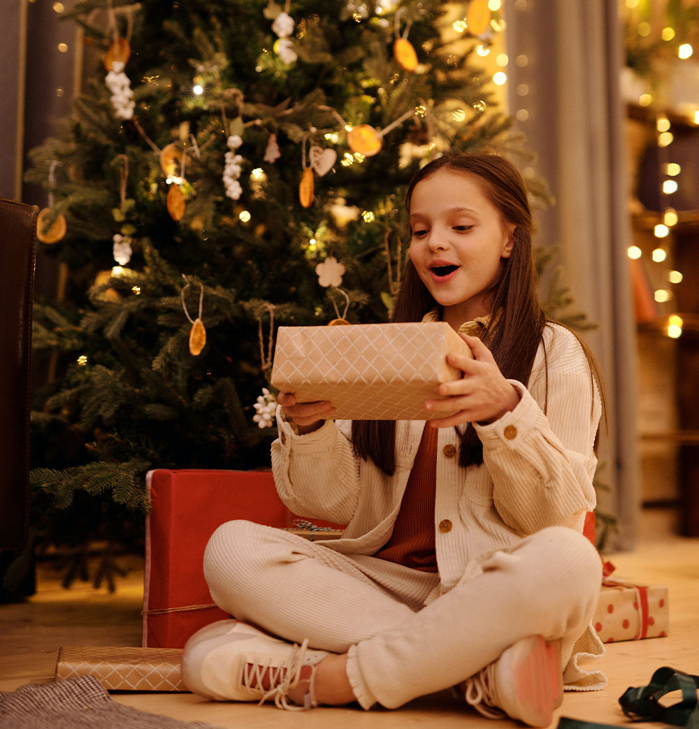 O fată se bucură de un cadou sub bradul de Crăciun.