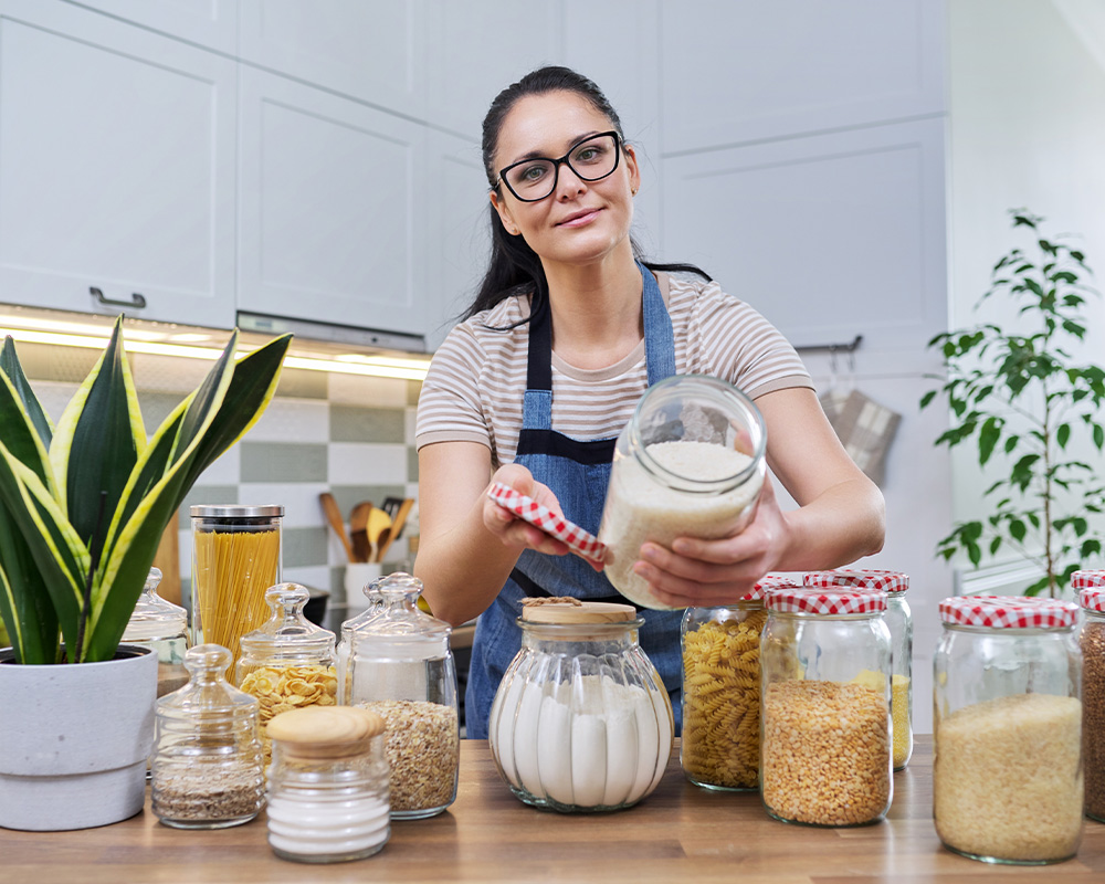 Femeia în bucătărie arată borcane pentru depozitarea alimentelor uscate
