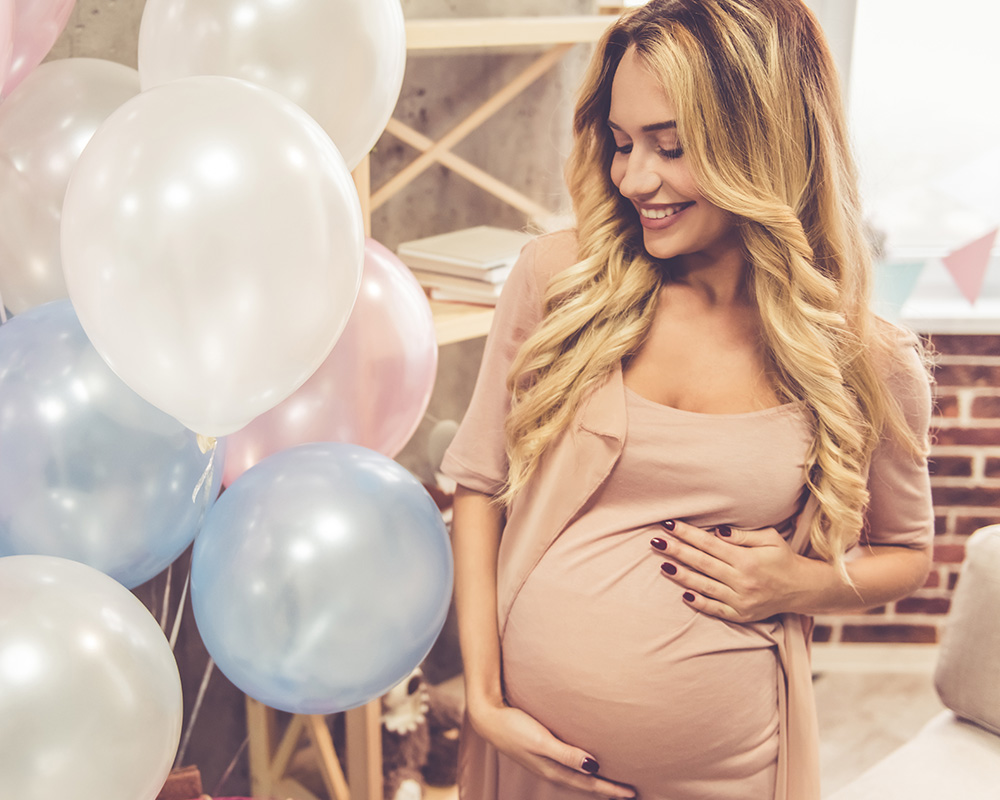O femeie însărcinată privește cu zâmbetul pe buze baloane colorate la petrecerea baby shower