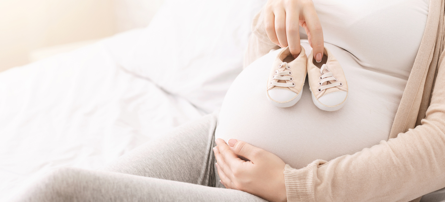 Femeia însărcinată ține pantofii pentru bebeluși pe burtica ei 