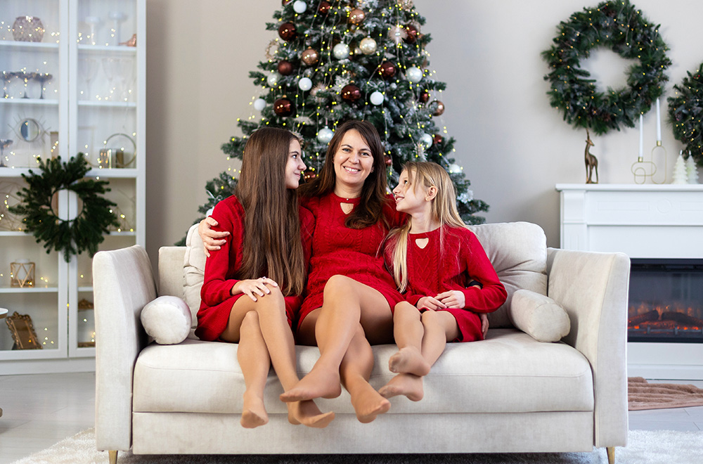 Mama și fiicele ei, îmbrăcate în rochii roșii, petrec timpul de sărbători împreună lângă brad.