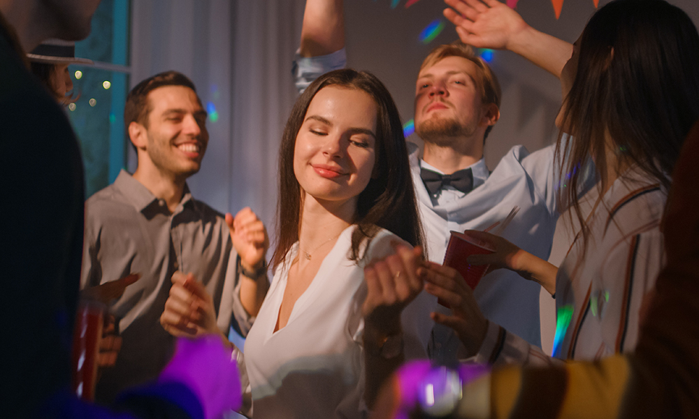 Un grup de oameni dansând la o petrecere, printre care o femeie care se bucură de muzică.